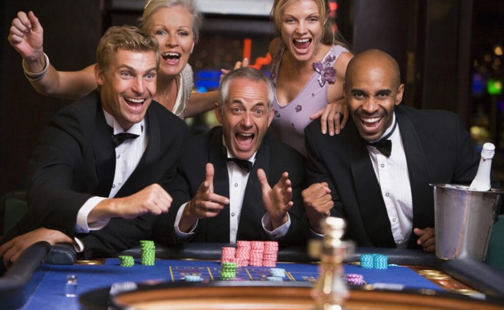 A group of friends celebrate at a casino roulette table.