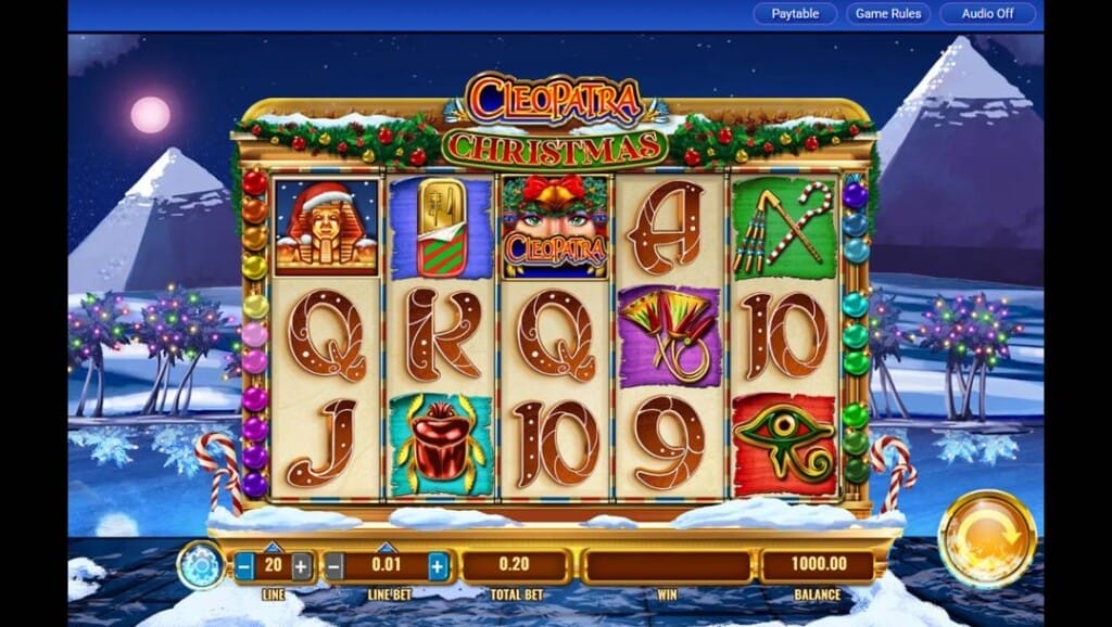 A screenshot of Cleopatra Christmas. The background of this slot has Egyptian pyramids, sand, and an oasis covered in snow. The palm trees are also covered in Christmas lights. In the foreground, the reels have Christmas decorations and feature a variety of Egyptian-themed symbols with a Christmas twist, as well as classic playing card symbols.