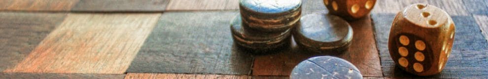 Old wooden dice on a checkered wooden board.