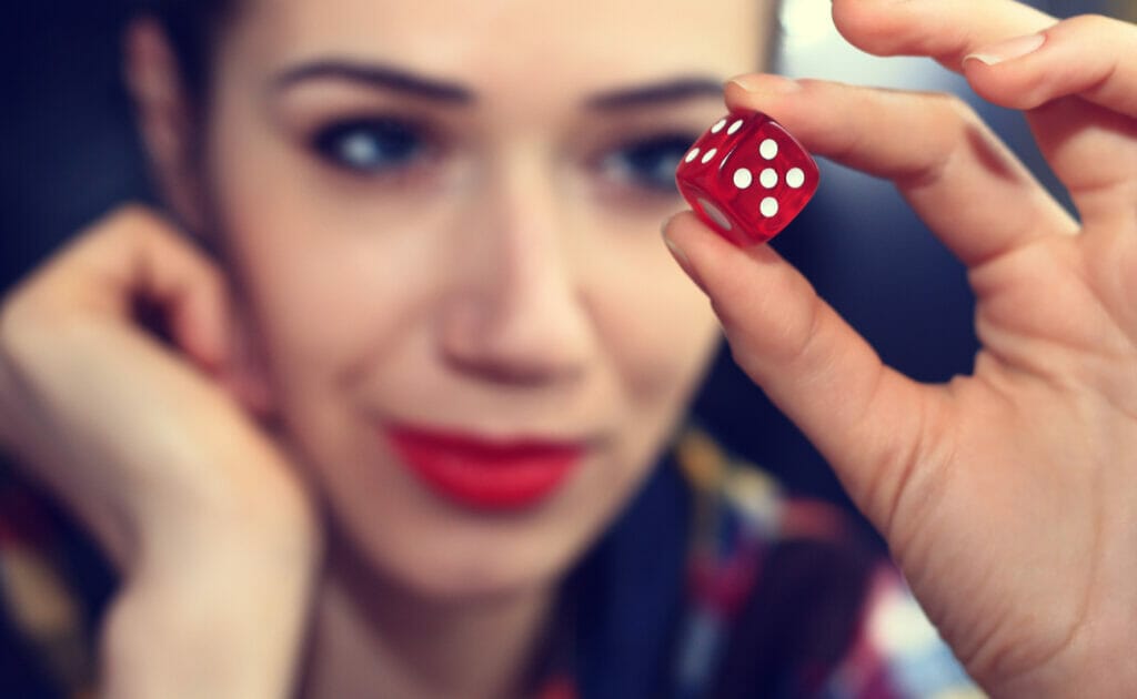 A woman holds up a red dice showing five.
