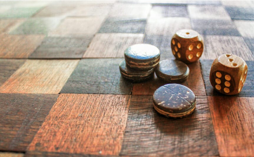 Old wooden dice on a checkered wooden board.
