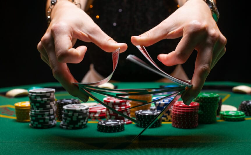 Close-up of a poker dealer shuffling cards with casino chips in the background.