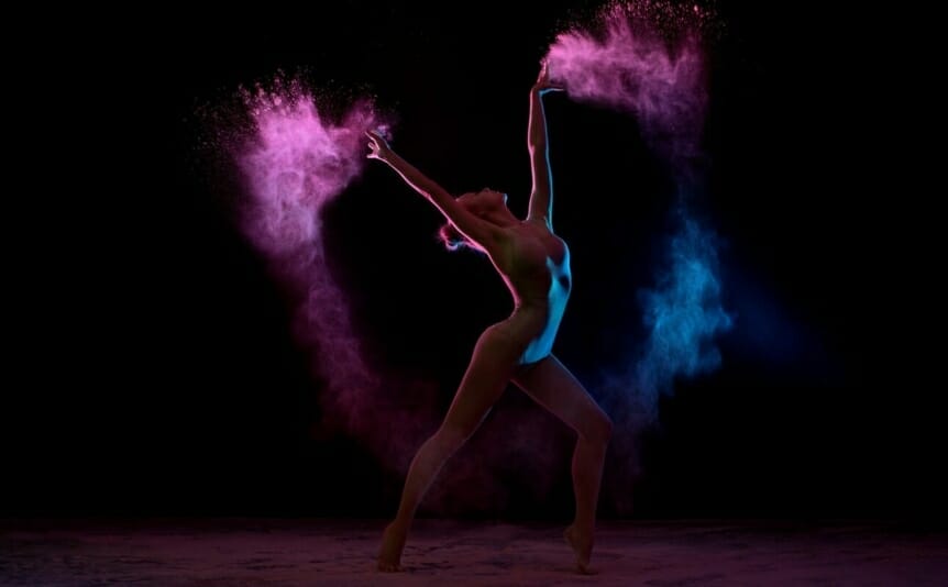 Acrobat dancing in color powder cloud against a black background.