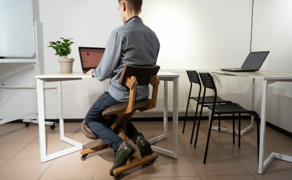 A man sits on a kneeling chair while he works at his desk.