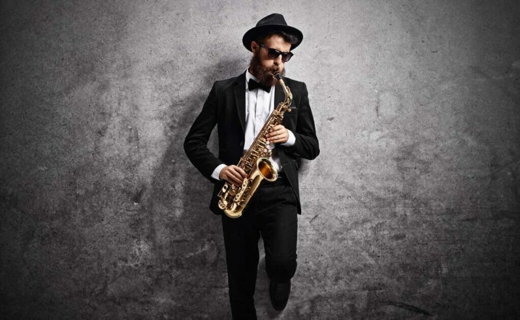 Jazz musician playing the saxophone and leaning against a gray wall.