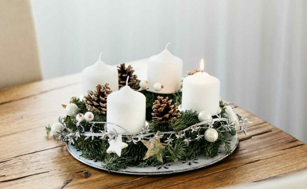 An advent wreath with white candles on a wooden table.