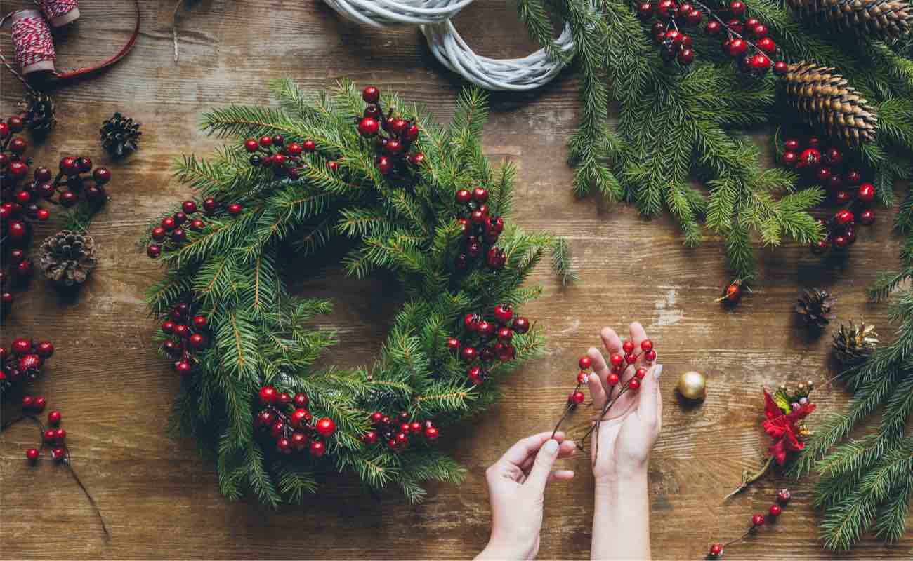 A woman making a Christmas wreath with pine branches and berries.