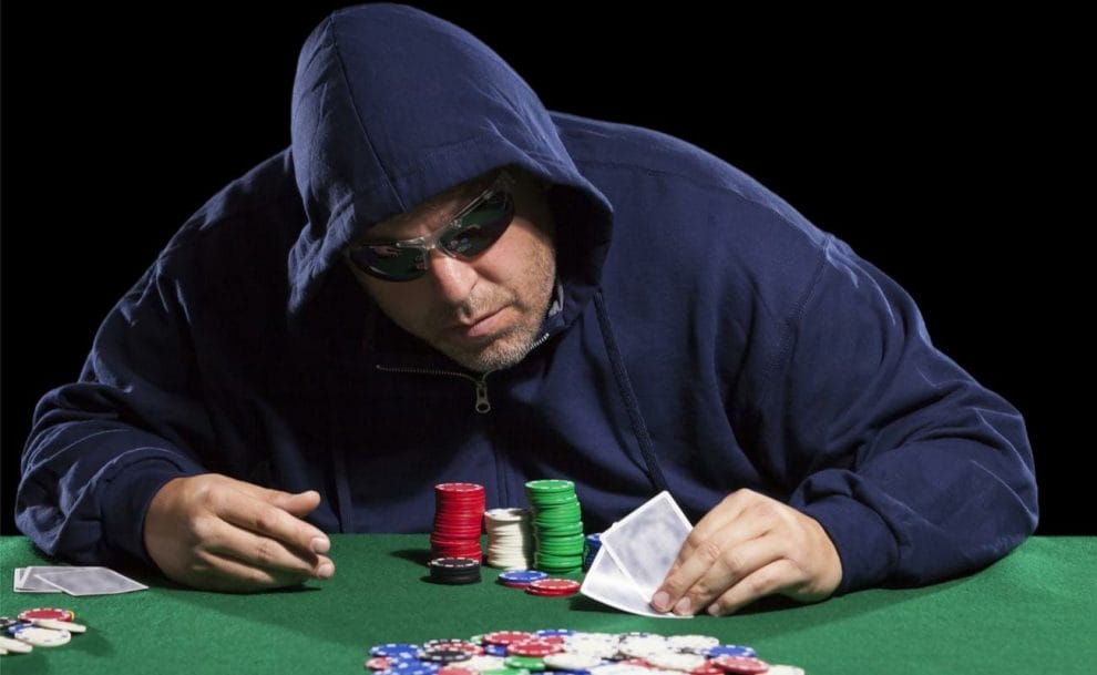 A poker player wearing a navy blue hoodie and sunglasses at the poker table.