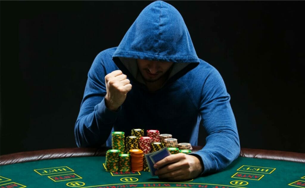 A poker player wearing a hoodie raising his fist in victory at the poker table.