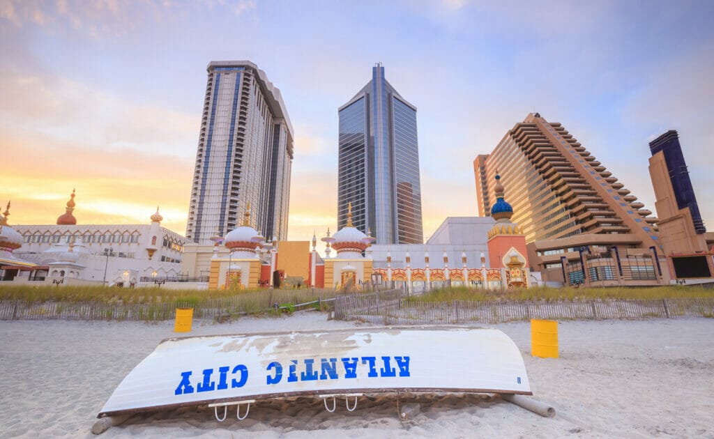 A white boat with “Atlantic City” in blue on the side, resting on the beach with high-rise resort buildings in the background.