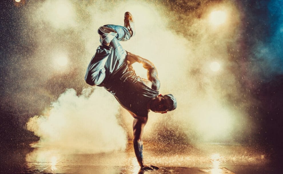 A young man with one hand on the floor while breakdancing with steam in the background.