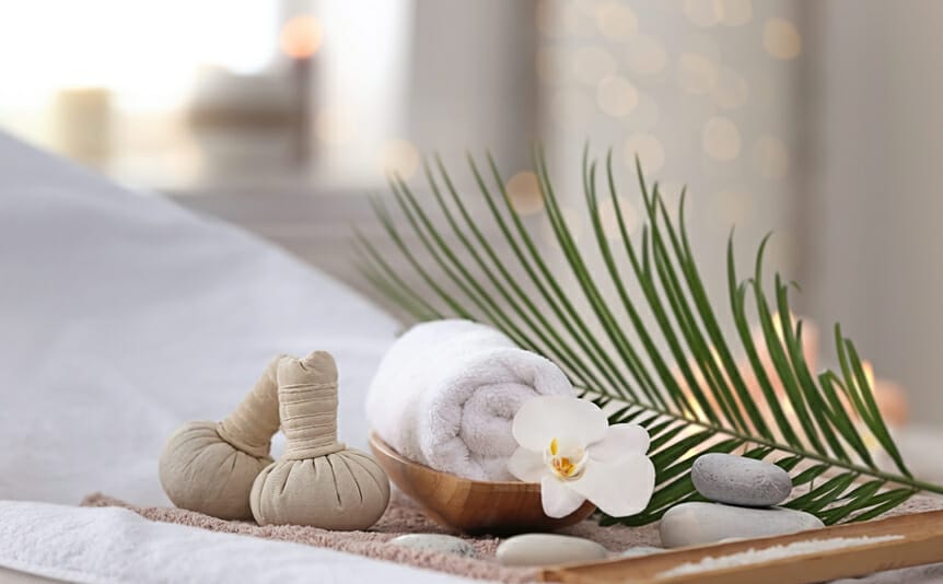 Composition of a variety of spa items on a massage table, as well as a flower and palm leaf.
