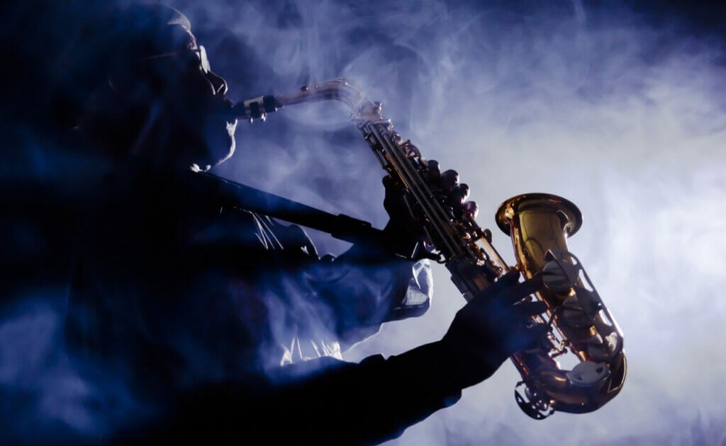 A performer playing the saxophone on a smokey stage.