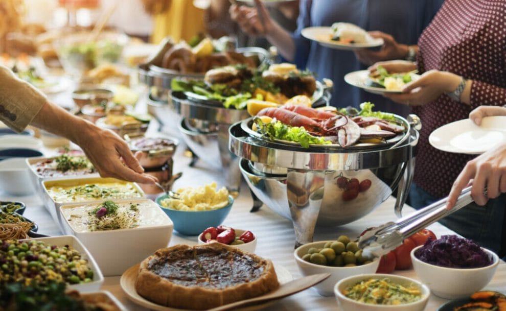 Close-up of people serving themselves at a buffet.