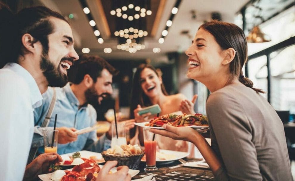A group of friends smiling as they eat at a restaurant.