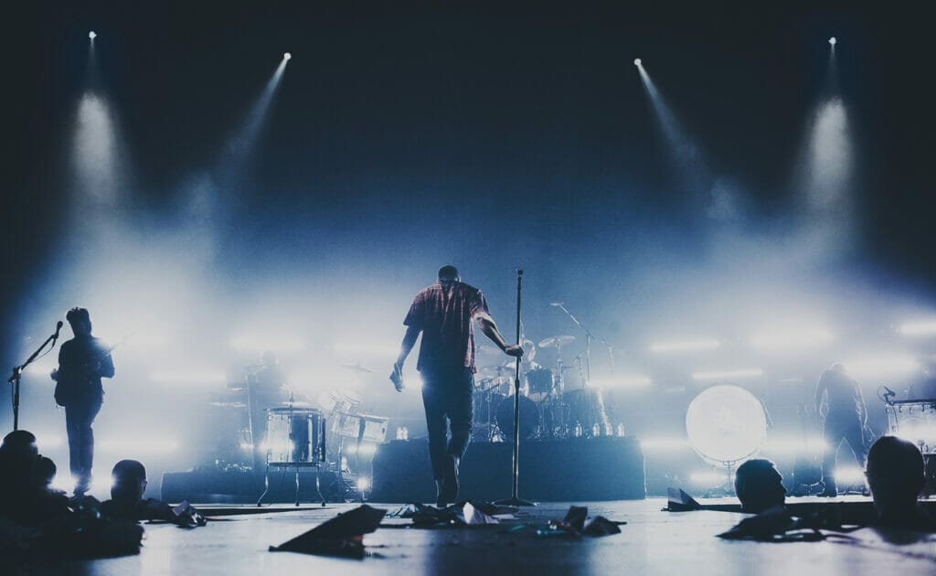 A back view of singers on stage with lights on them facing the audience.