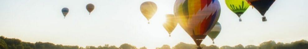 Hot-air balloons taking off at sunrise over a lush green field.