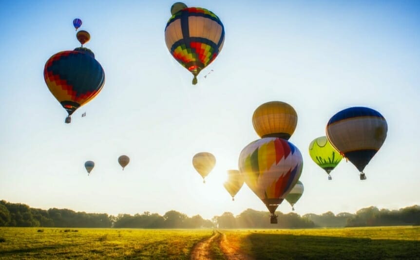 Hot-air balloons taking off at sunrise over a lush green field.