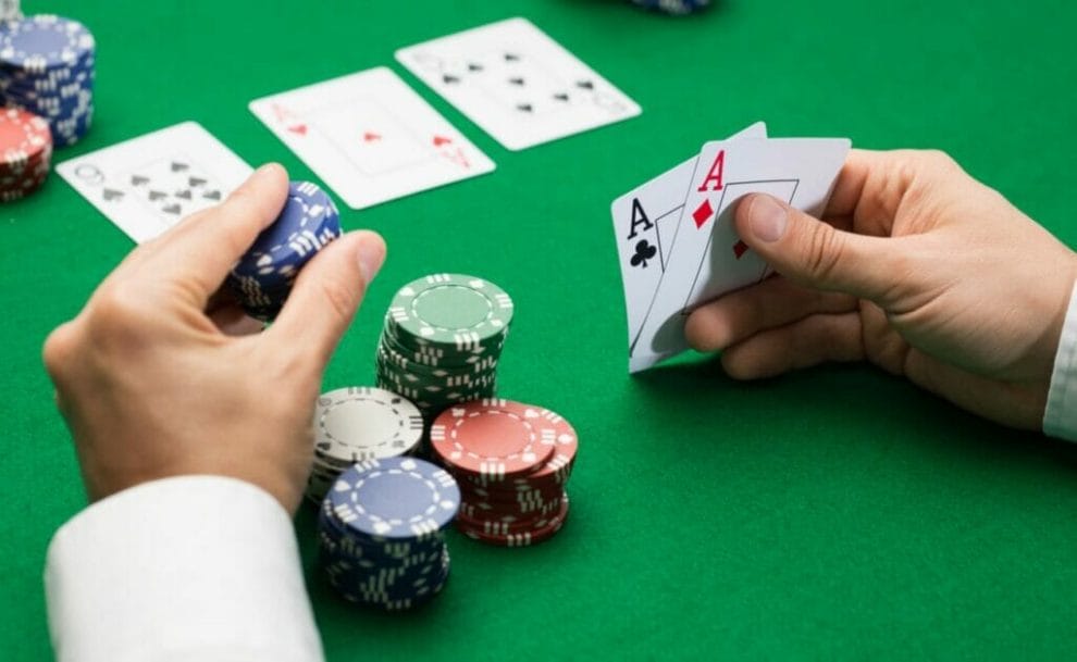 A bettor with a stack of chips holds two Aces over the felt while about to place a bet.