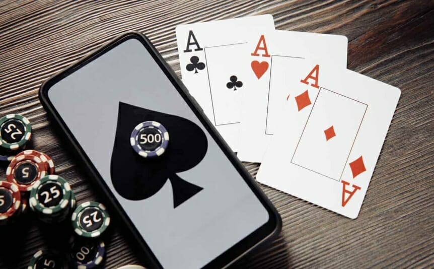 Casino chips, playing cards and a mobile phone featuring a spade symbol on a table.