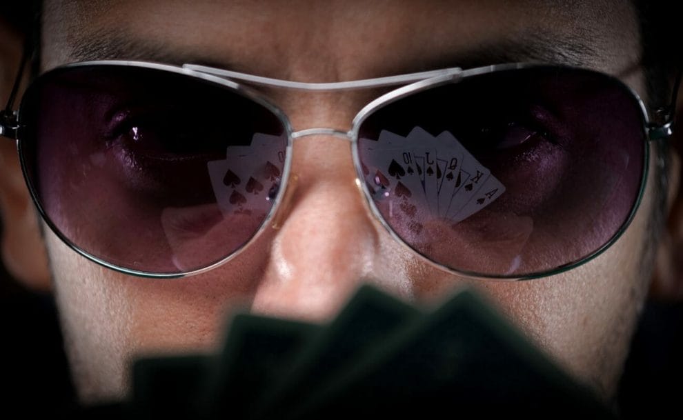 A man wearing sunglasses and looking at playing cards.