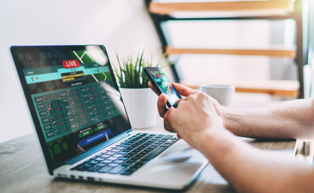 A man sports betting on his phone and laptop.