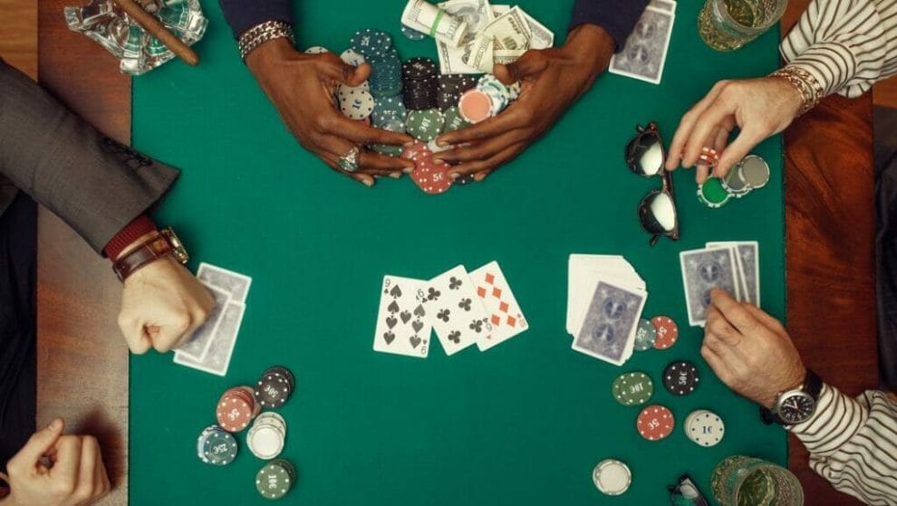  A man pulls a huge pile of poker chips towards him, while another player clenches his fist and another plays with his poker chips.