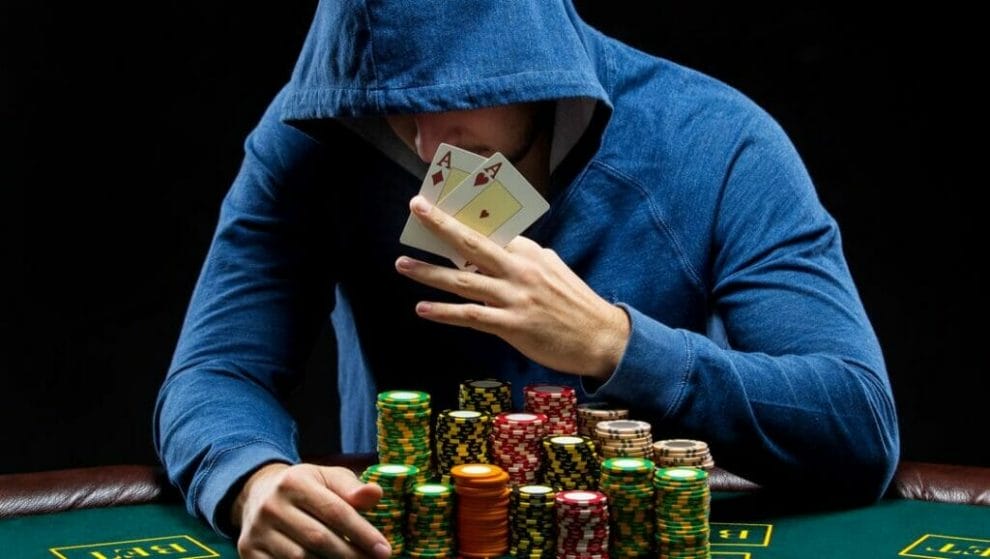 A poker player wearing a hoodie with massive stacks of poker chips reveals a pair of aces.