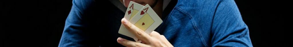 A poker player wearing a hoodie with massive stacks of poker chips reveals a pair of aces.