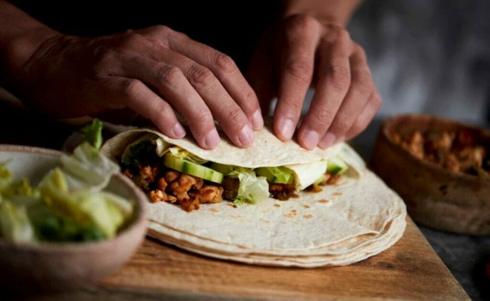 Close-up of a man folding a tortilla into a burrito.
