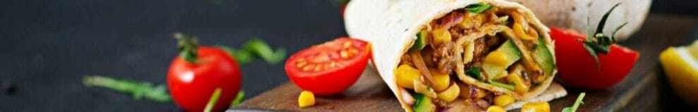 Burritos on a wooden board surrounded by sliced tomatoes.