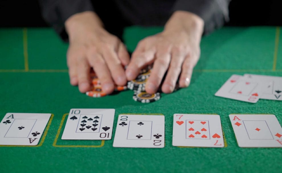 A man puts his hands over the chips with the community cards in front of him on a poker table.