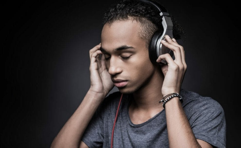A serious young man listening to music through headphones on a black background.