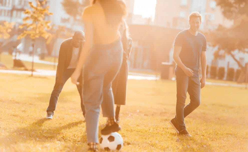 A group of friends playing soccer in the park at sunset.