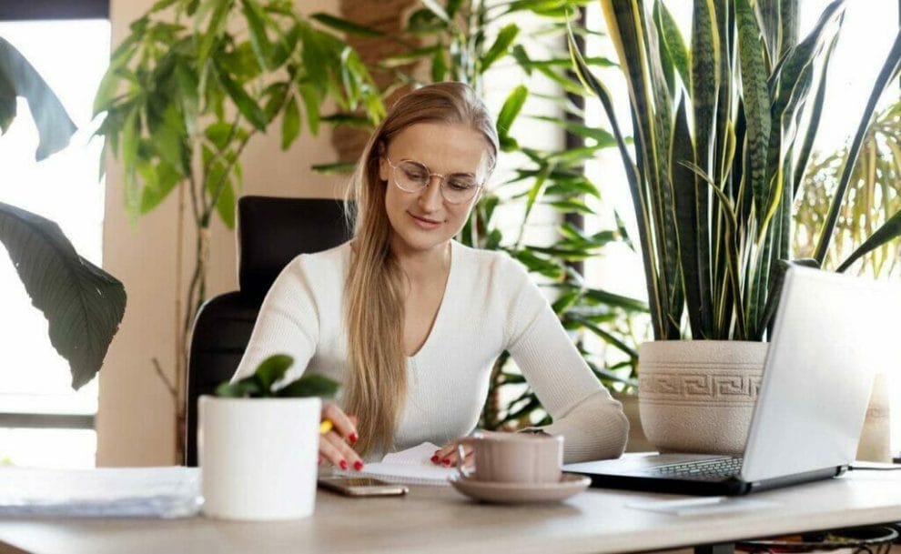 A woman works at a desk surrounded by plants.