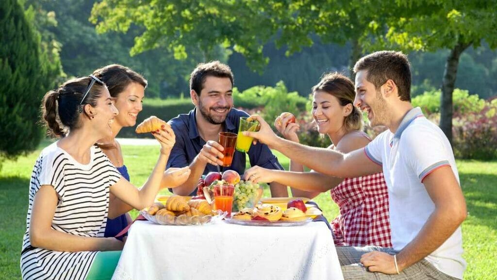 A group of smiling people enjoy an alfresco meal in the garden.