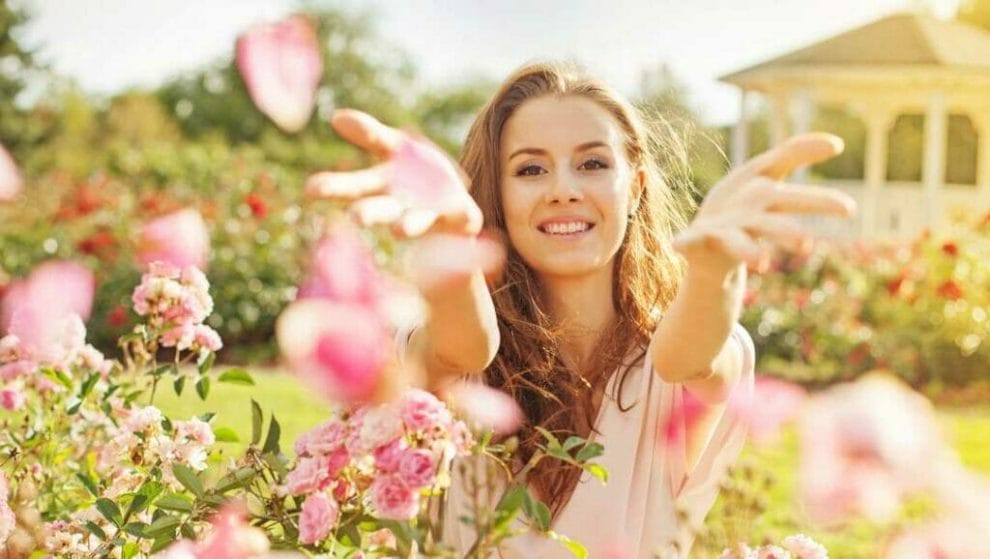 A smiling woman throws pink flower petals into the air.