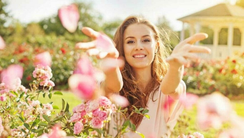 A smiling woman throws pink flower petals into the air.  