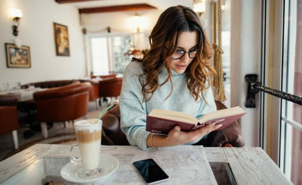 A woman reading a book while at a cafe.