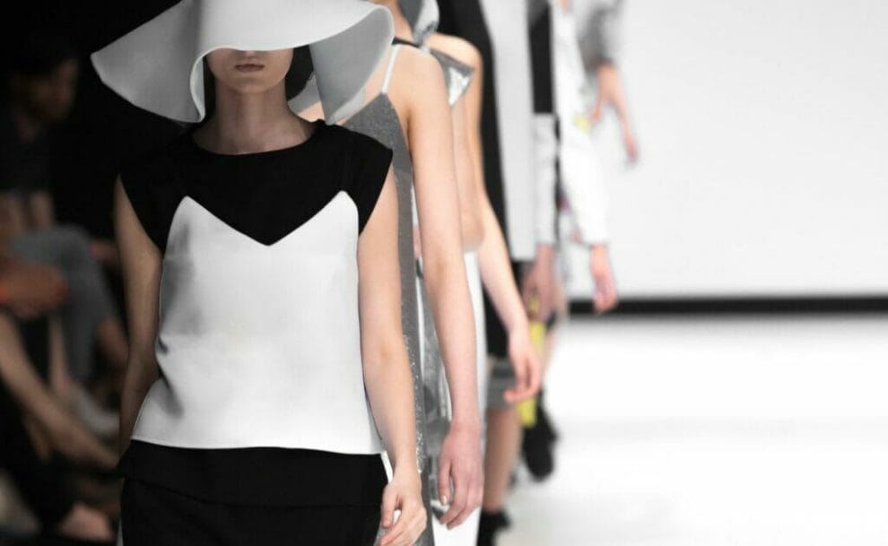 Women with white hats walking down the fashion runway in a straight line.