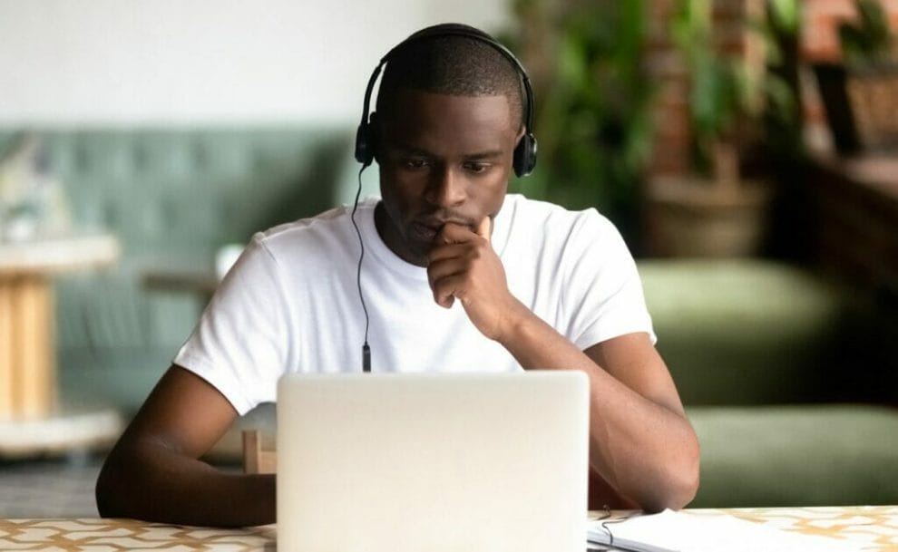 A focused man looking at his laptop screen with headphones on.