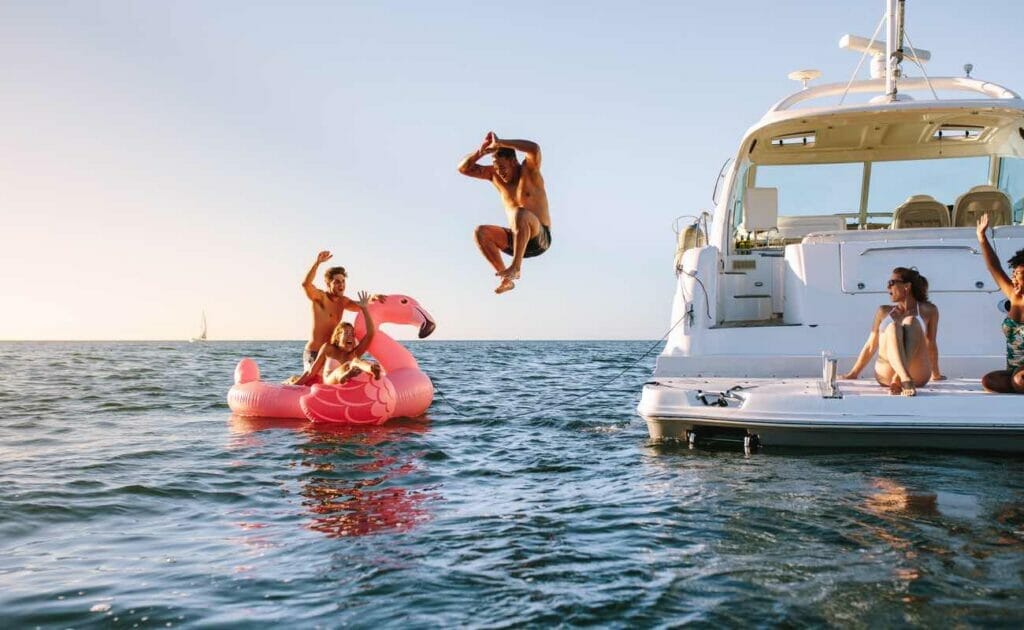 People swimming in the sea and jumping off the side of a yacht.