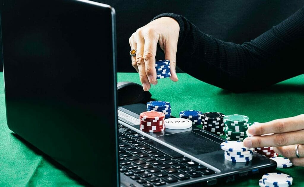 A woman plays with poker chips while using her laptop computer.