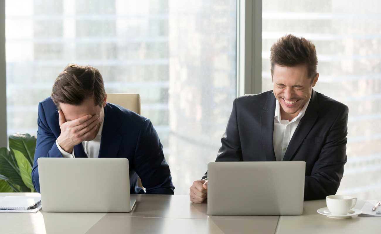 Two men sitting in front of laptops laughing.