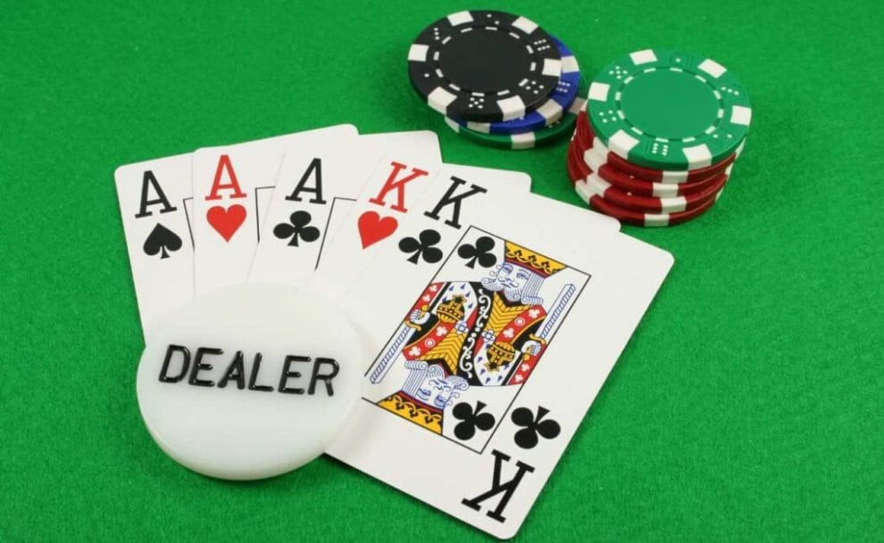 A dealer chip on top of Three Aces and two Kings with two short stacks of poker chips on top of a green, felt table.