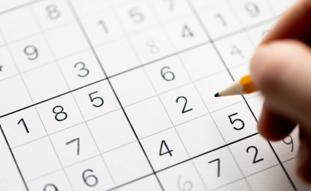A person fills out a sudoku game with a pencil.