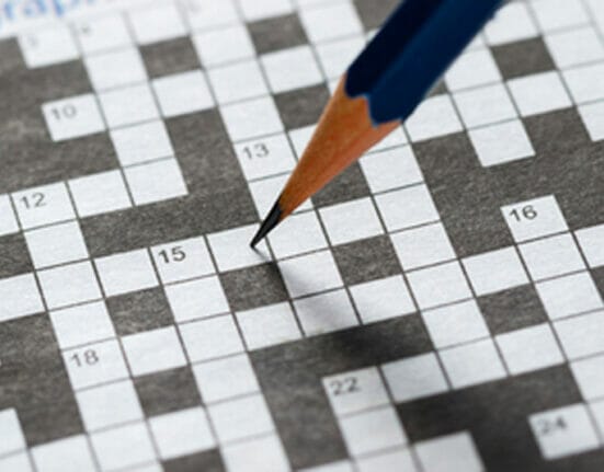 Someone filling out a crossword puzzle with a pencil.