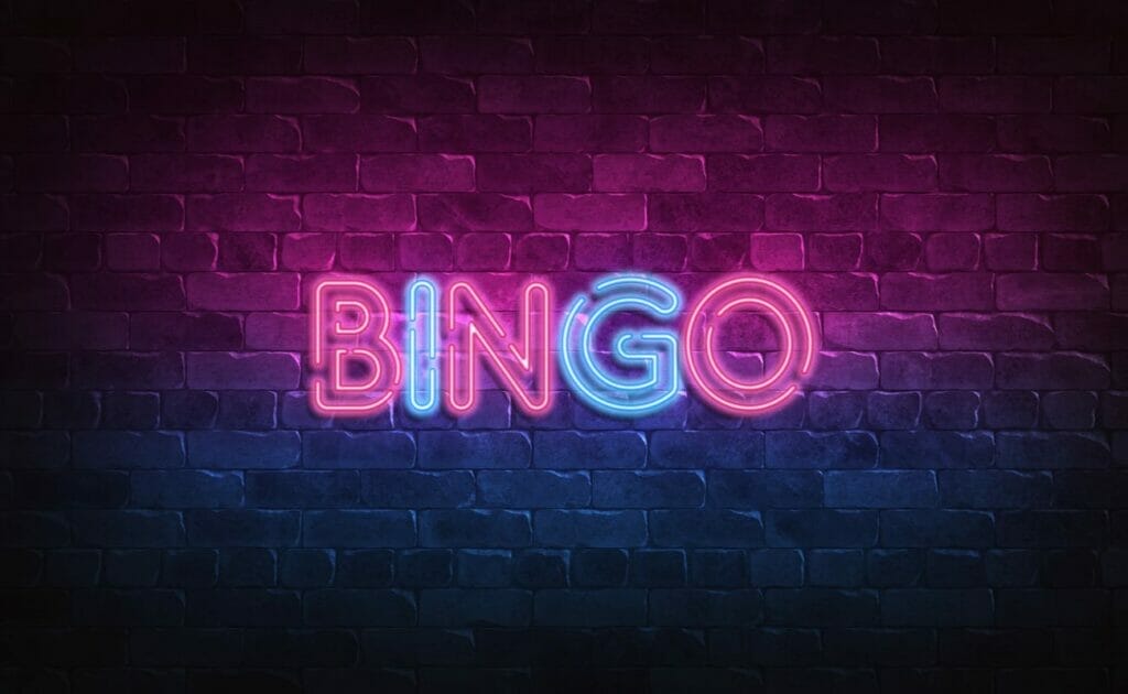 A neon-lit “BINGO” sign hanging on a brick-face city wall.