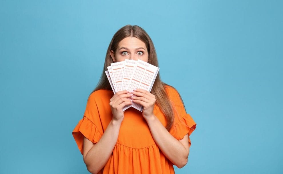 A woman with a surprised look on her face holding up lotto tickets, isolated against a blue background.