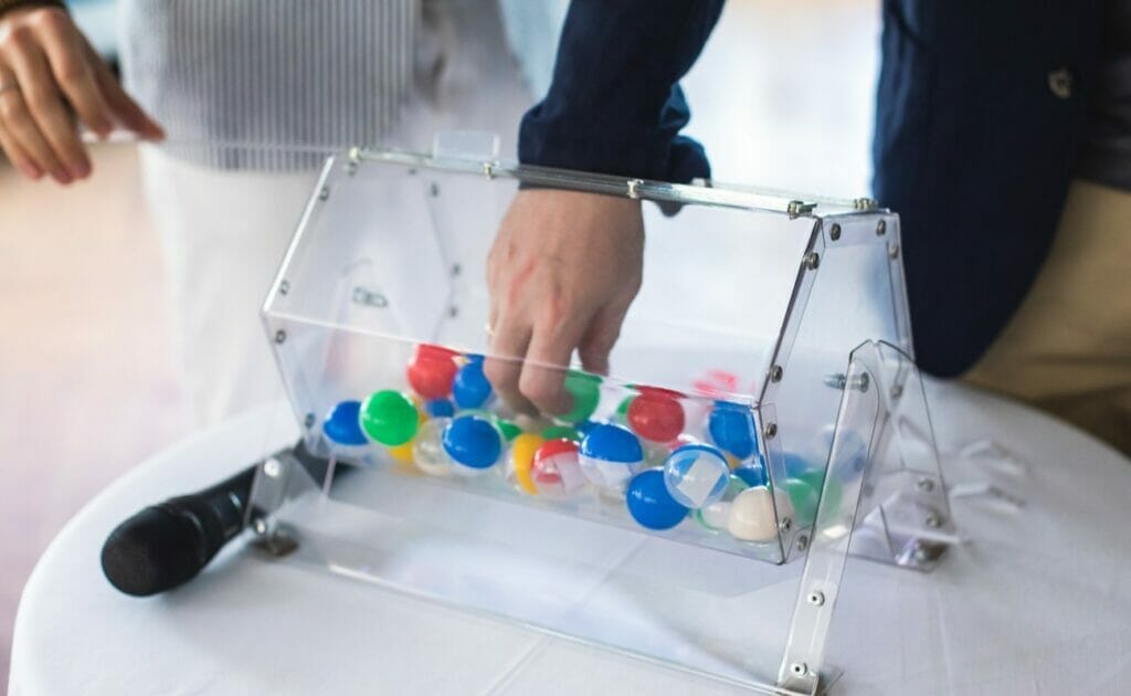 A person grabs a bingo ball from inside a plastic bingo cage.